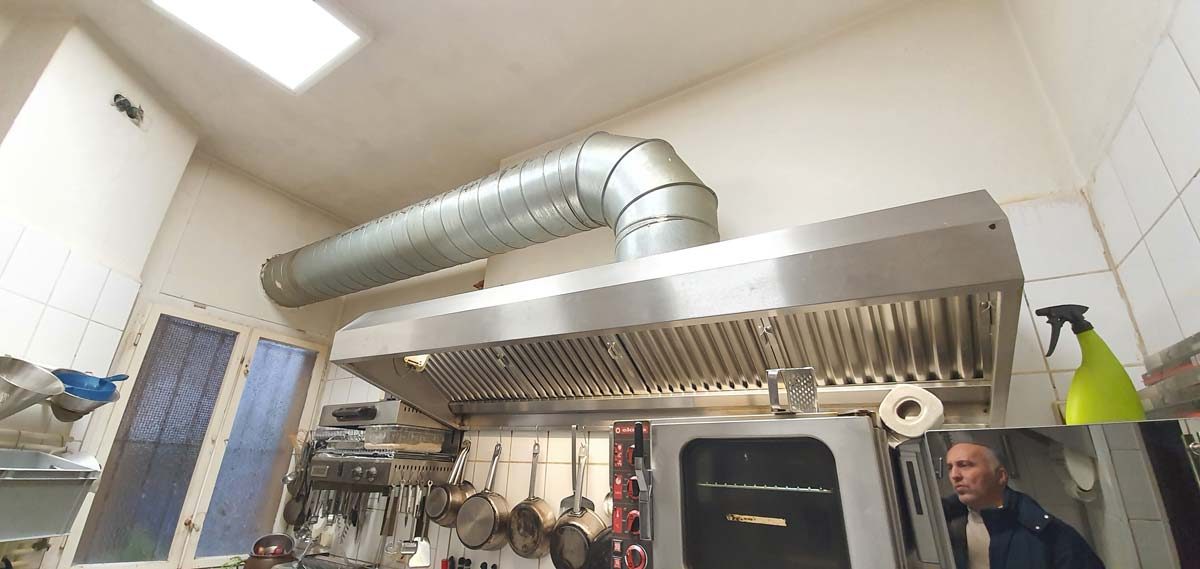 Installation einer Edelstahl-Dunsthaube mit Wickelfalzrohr-Abluftsystem in einer gewerblichen Küche.