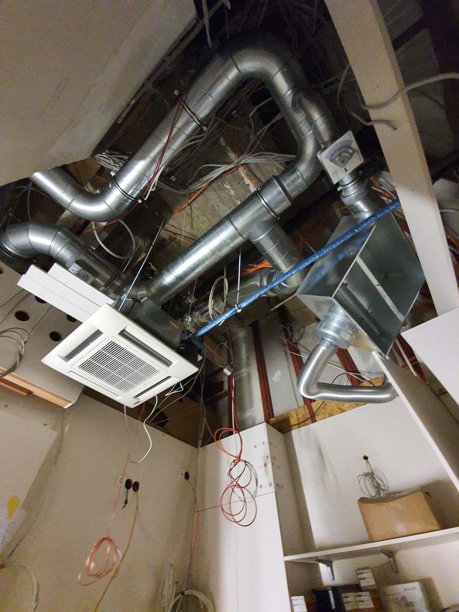 Installation einer Klimaanlagen-Deckenkassette mit zugehöriger Luftkanal- und Kältemittelleitungsführung in einem Rohbau.